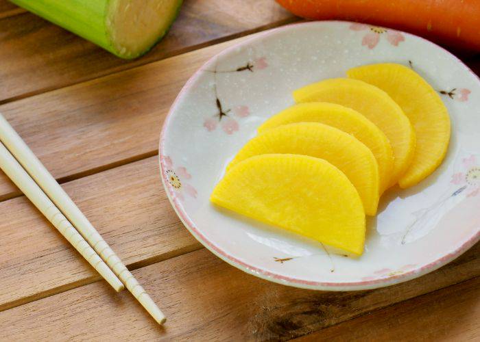 Bright yellow radish on a plate with a set of chopsticks next to them.